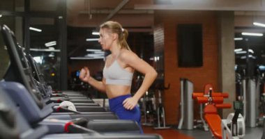 Genç bir kadın spor salonunda koşu bandında koşuyor.