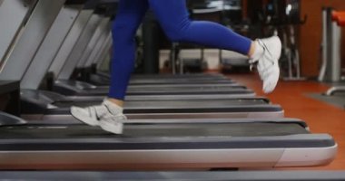 Genç bir kadın spor salonunda koşu bandında koşuyor.