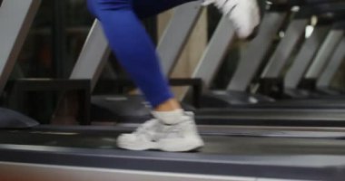 Bir kadın koşu bandında koşuyor, spor salonunda egzersiz yapıyor, kadın bacakları yakın plan.
