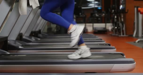 Bir kadın koşu bandında koşuyor, spor salonunda egzersiz yapıyor, kadın bacakları yakın plan. — Stok video