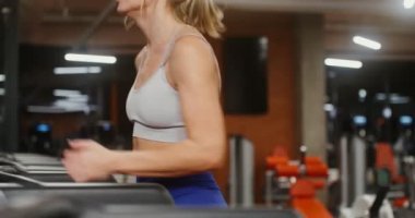 Genç bir kadın spor salonunda koşu bandında koşuyor.