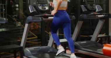 Genç bir kadın spor salonunda koşu bandında koşuyor.
