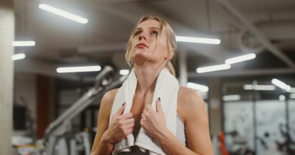 Mujer joven cansada después del entrenamiento, mirando a la cámara mientras está de pie en el gimnasio — Vídeo de stock