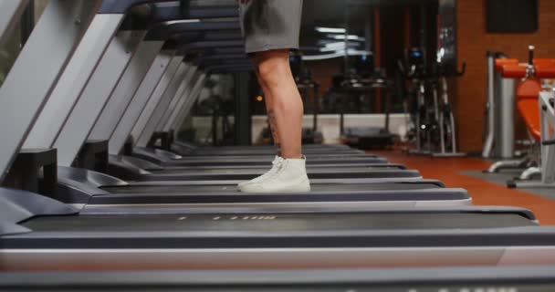 A sportoló elkezdi a futópad edzését, a férfi lábak közelednek. — Stock videók