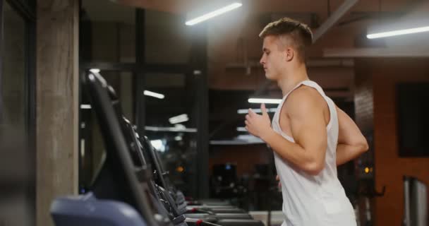 Een jongeman met een Europees uiterlijk die op een loopband in de sportschool loopt — Stockvideo