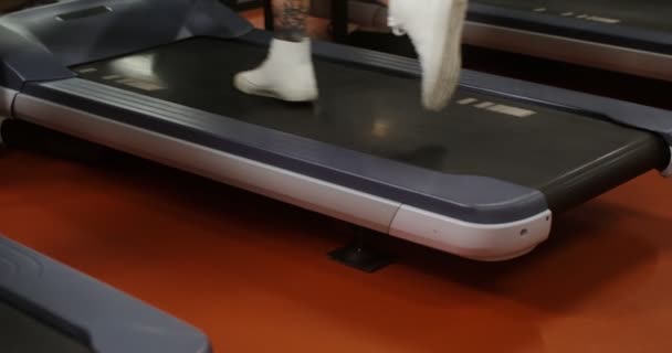 A young man of European appearance running on a treadmill in the gym — Stockvideo