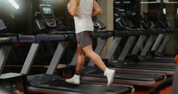 Um jovem de aparência europeia correndo em uma esteira no ginásio — Vídeo de Stock
