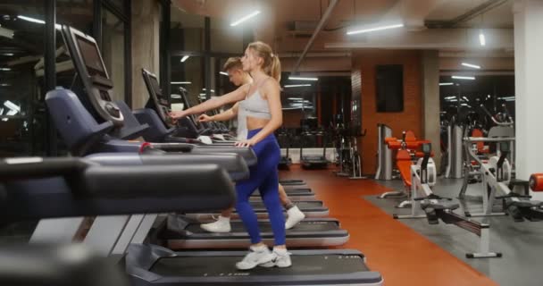 Young man and woman run on a treadmill, working out in a modern gym together — Video Stock