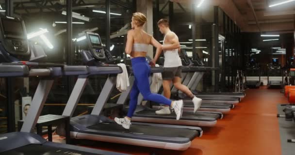 Młody mężczyzna i kobieta biegają na bieżni, ćwicząc razem w nowoczesnej siłowni — Wideo stockowe