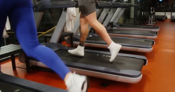 Jongeman en vrouw rennen op een loopband, trainen in een moderne fitnessruimte samen — Stockvideo