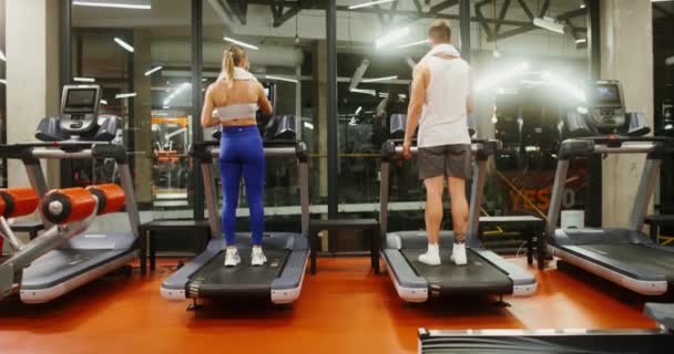 Young man and woman run on a treadmill, working out in a modern gym together — Stock Video