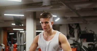 Genç adam, modern bir spor salonunda egzersiz makinesinde bisepsi eğitiyor.