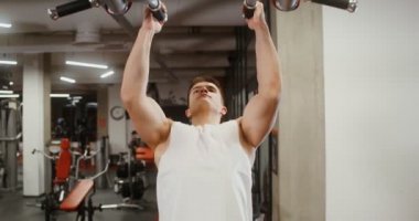 Modern bir spor salonunun simülatöründe barfiks çeken genç bir adamın ön görüntüsü.