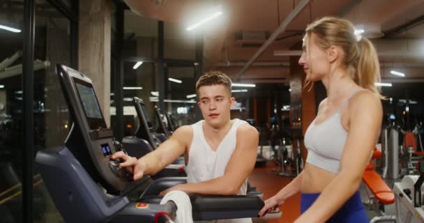 Treinador escolhe um modo de treino em uma esteira para uma jovem mulher no ginásio moderno — Vídeo de Stock