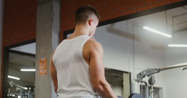 A young man trains biceps, lifting a dumbbell with one hand in the gym — Stock Video