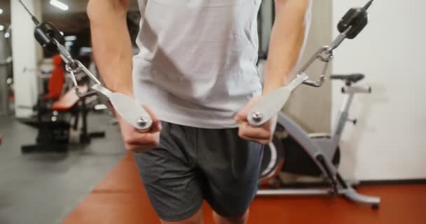 Genç adam, modern bir spor salonunda egzersiz makinesinde bisepsi eğitiyor. — Stok video