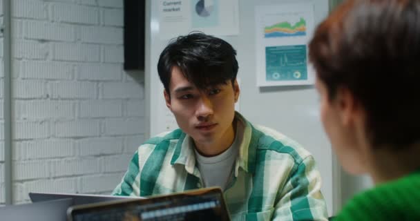 Mladý muž asijského vzhledu komunikuje s kolegy sedícími v kanceláři — Stock video