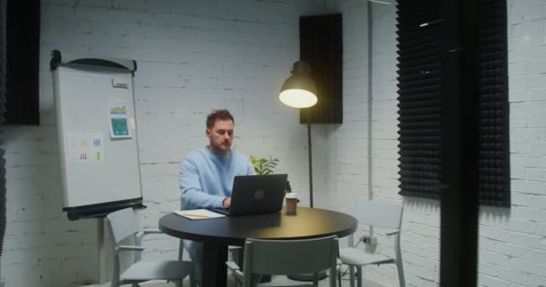 A young woman enters the meeting room where her colleague is working on a laptop — Vídeo de Stock