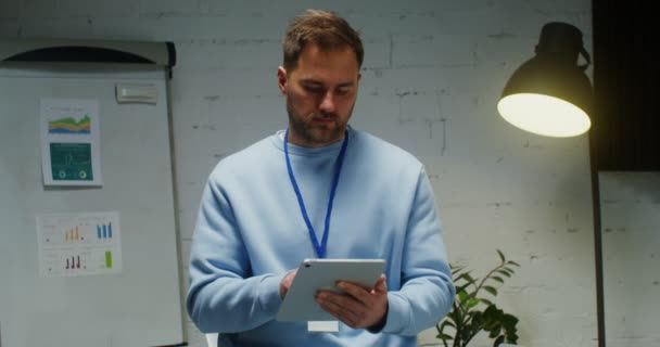 Un hombre sonríe mirando a la cámara, interrumpido del trabajo en la tableta en la oficina — Vídeos de Stock