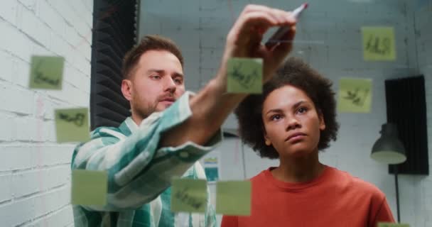 Un jeune homme et une jeune femme planifient dans le bureau, en dessinant sur une planche de verre — Video