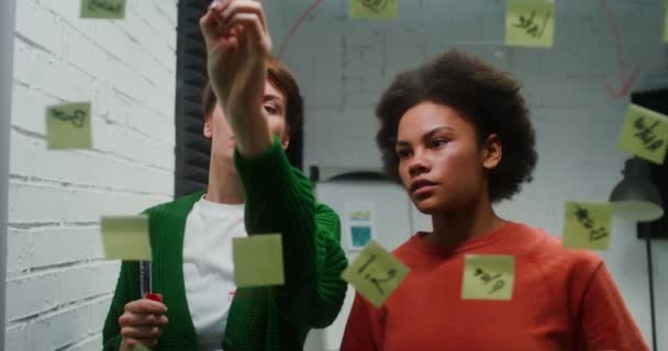 A woman is drawing a business strategy on a glass board working with assistant — Video Stock