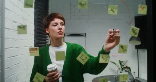 Молода жінка займається плануванням використання скляної дошки, яка працює сама в офісі — стокове відео