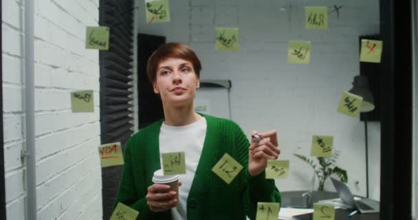 Young woman is engaged in planning using glass board working alone in office — Stockvideo