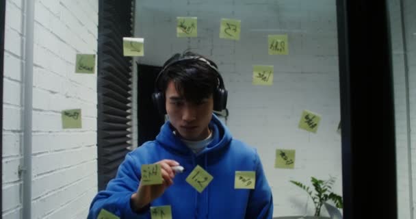 Jeune homme écoute de la musique dans les écouteurs et la planification sur le mur de verre — Video