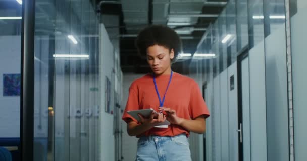 Een jonge Afro-Amerikaanse vrouw gebruikt een tablet en kijkt naar de camera in het kantoor — Stockvideo
