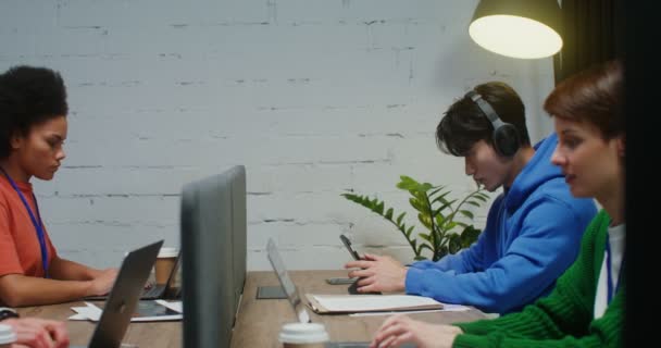 A men and women work at laptops, sitting at one work desk in a office — Stockvideo