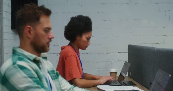 Un hombre y una mujer trabajan en computadoras portátiles, sentados en un escritorio en una oficina — Vídeos de Stock