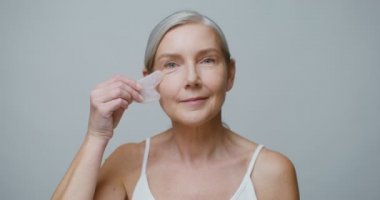 Gua Sha taşı kullanarak yüz masajı yapan yaşlı bir manken.