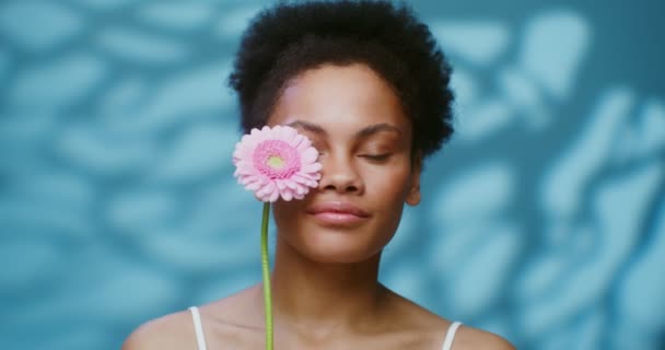 A young African American model poses looking at the camera with gerbera flower — 图库视频影像