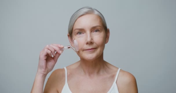 Um modelo idoso fazendo uma massagem facial usando um rolo de jade — Vídeo de Stock