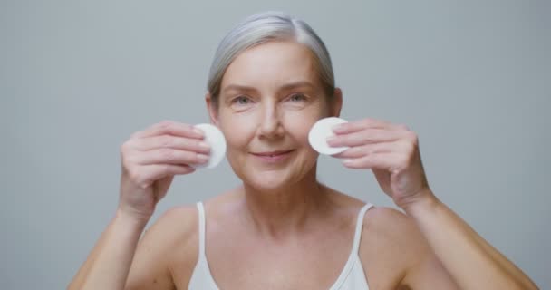 Older model wipes her make-up with cotton pads and smiling looking into camera — Stockvideo