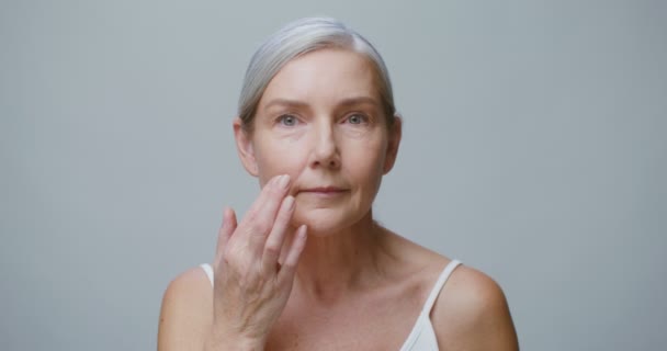 En äldre modell applicerar fuktighetskräm i ansiktet samtidigt som hon ler mot kameran — Stockvideo