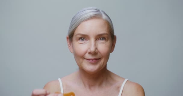 An elderly model applies patches under her eyes while smiling at the camera — 图库视频影像