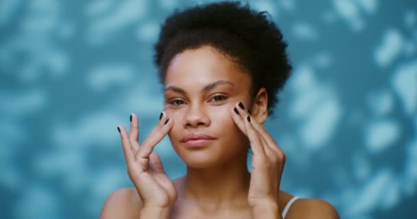 Sensual young African American woman applying moisturizer to her face — Stockvideo