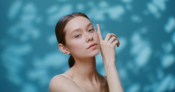 Una joven modelo sin maquillaje posando en un estudio tocando su cara — Vídeos de Stock
