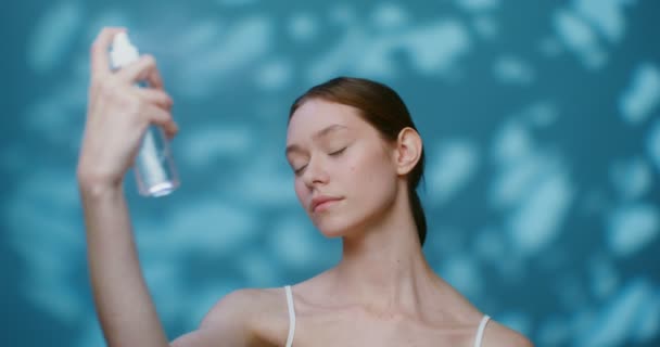 Een jonge blanke model zonder make-up spuit vloeistof uit een fles op haar gezicht — Stockvideo