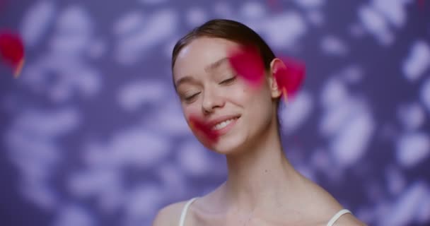 A young model smiling looking into camera standing against falling rose petals — ストック動画