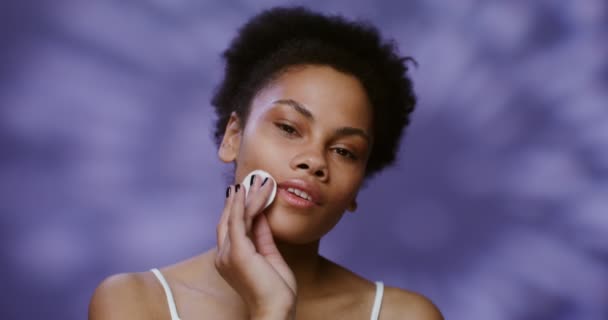 Seorang model Afrika-Amerika dengan lembut menghapus makeup dari wajahnya dengan pad kapas — Stok Video