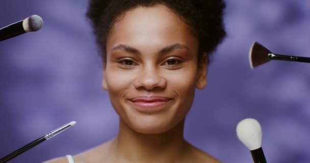 African American model standing, between makeup brushes pointed towards her — Wideo stockowe