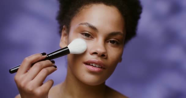 Young African American gently brushing makeup brush across her face — 图库视频影像