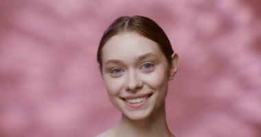 Makyajsız beyaz model kameraya bakıp gülümsüyor.