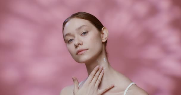 A model rubs moisturizer into the skin of her neck and looks at camera — Wideo stockowe