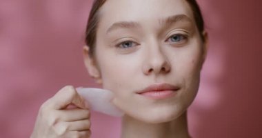 Gua Sha taşıyla yüz masajı yapan genç bir kadının yüzü.