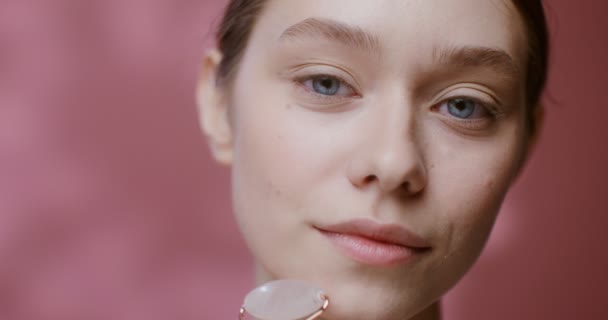 Il viso di una giovane donna che fa un massaggio facciale con un massaggiatore a rullo di giada — Video Stock