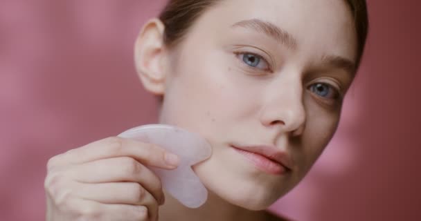 Gua Sha taşıyla yüz masajı yapan genç bir kadının yüzü. — Stok video