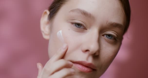 A model applies moisturizer to her neck and looks at the camera — Stockvideo